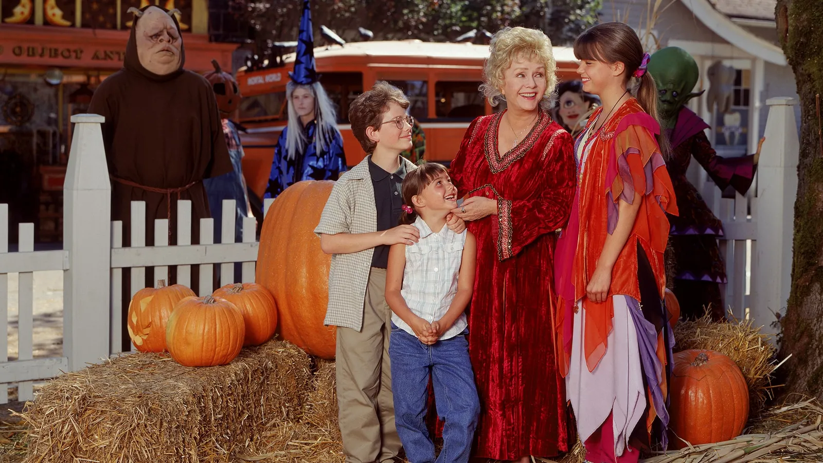 The Halloweentown family stands beside pumpkins, with costumed townspeople behind them.