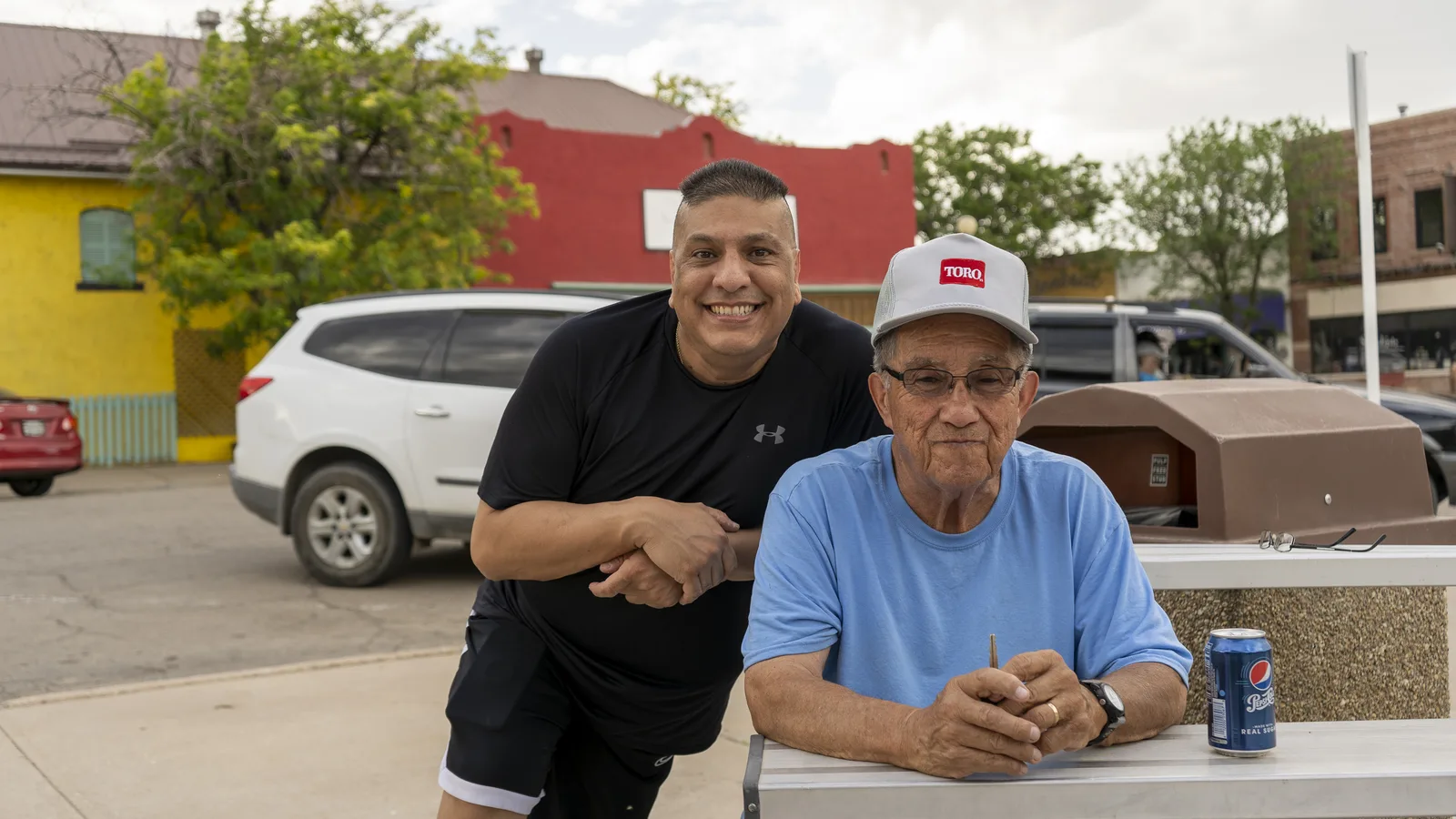 Two neighbors gather beside a picnic table at an outdoor community event.