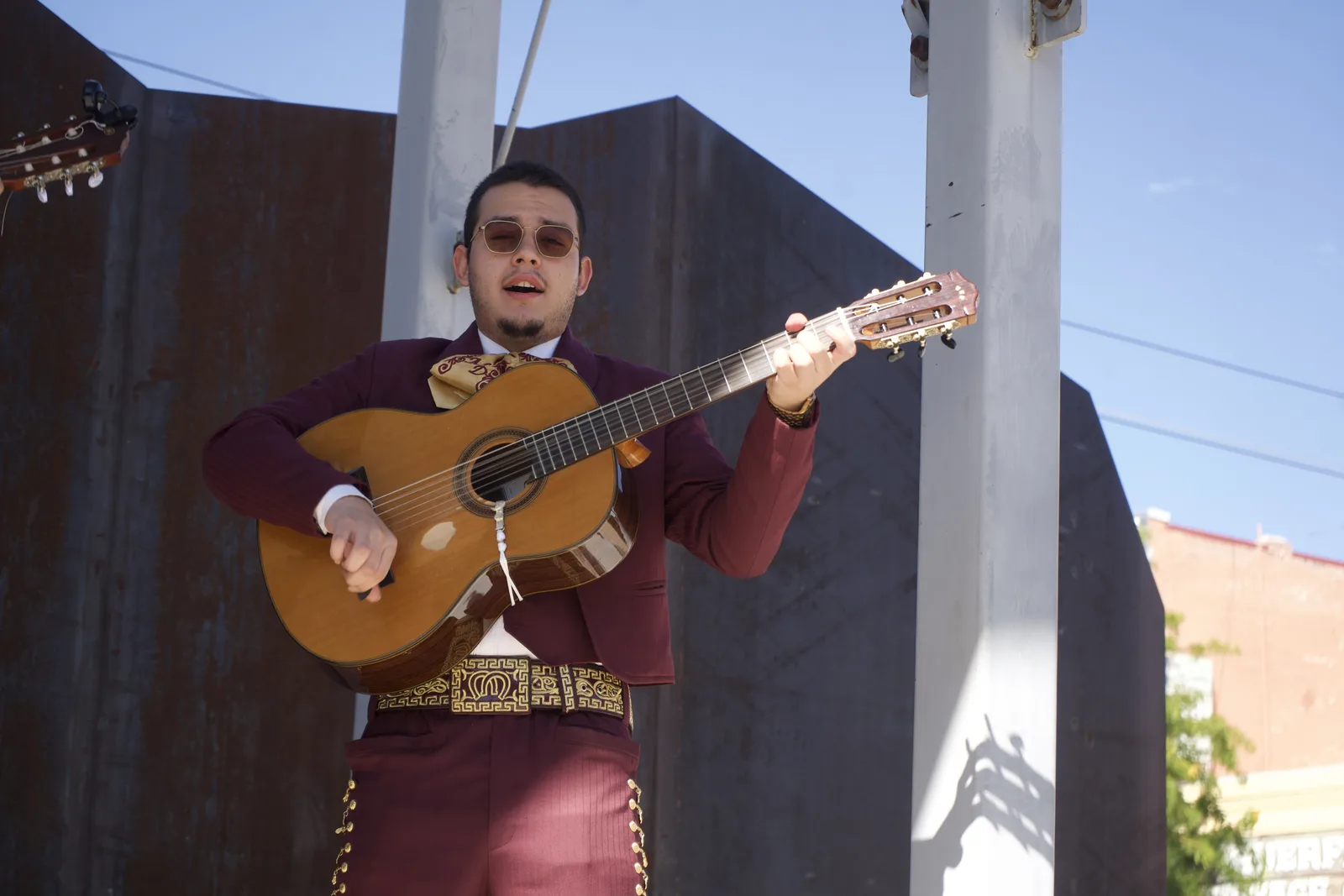 A mariachi musician sings while playing guitar on an outdoor stage.