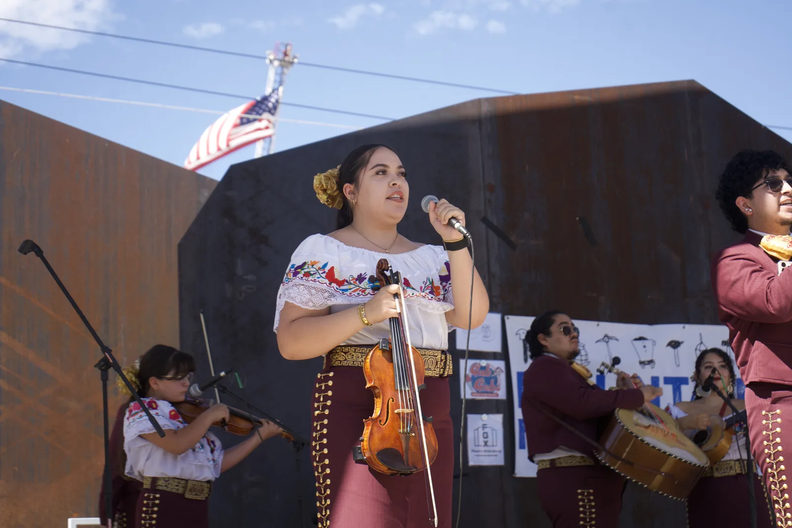 A mariachi violinist sings into a microphone during an outdoor performance.