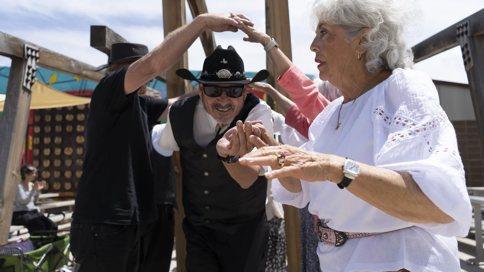 Community dancers raise their arms to form an arch during an outdoor performance.