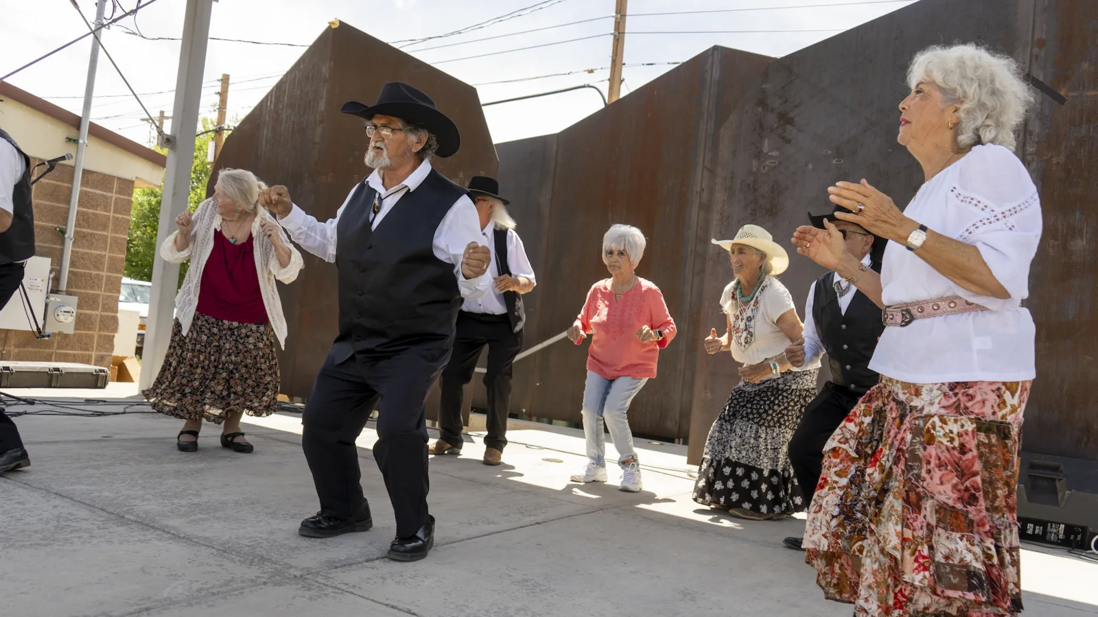 Adults in Western clothing perform an outdoor group dance.