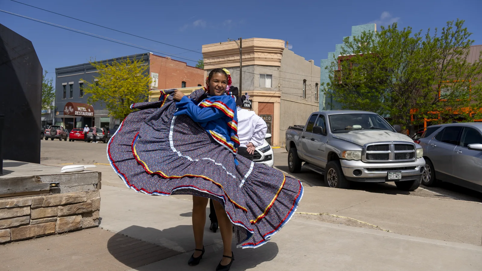 A folklórico dancer lifts a blue skirt while performing on a downtown sidewalk.