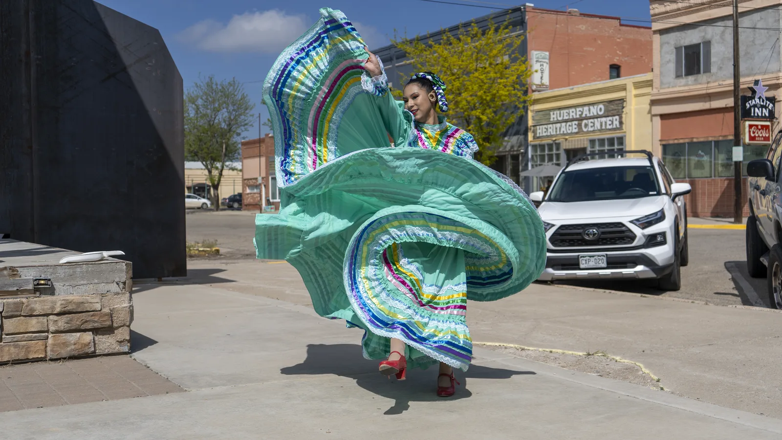 A folklórico dancer lifts a green skirt while performing outdoors in downtown Walsenburg.