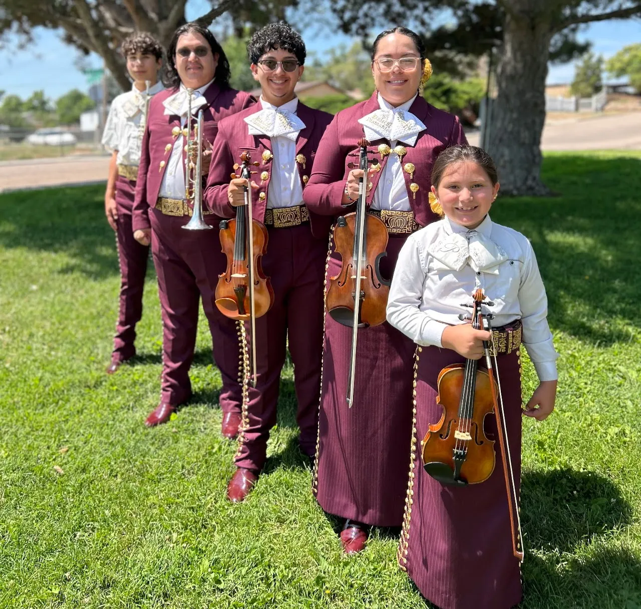 Mariachi Diamante musicians stand together on a lawn with violins and trumpet.