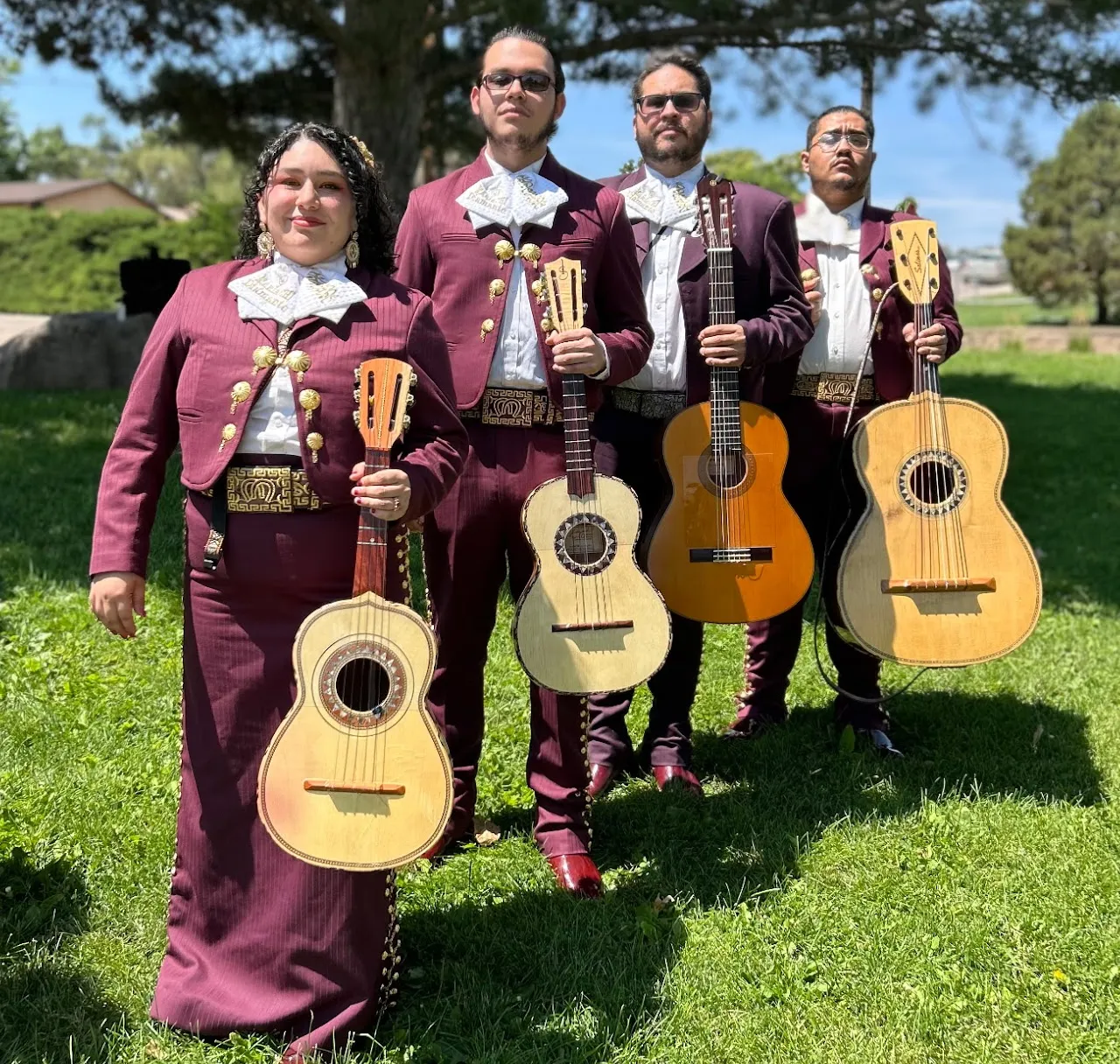 Four Mariachi Diamante musicians pose outdoors with guitarrón, vihuela, and guitars.