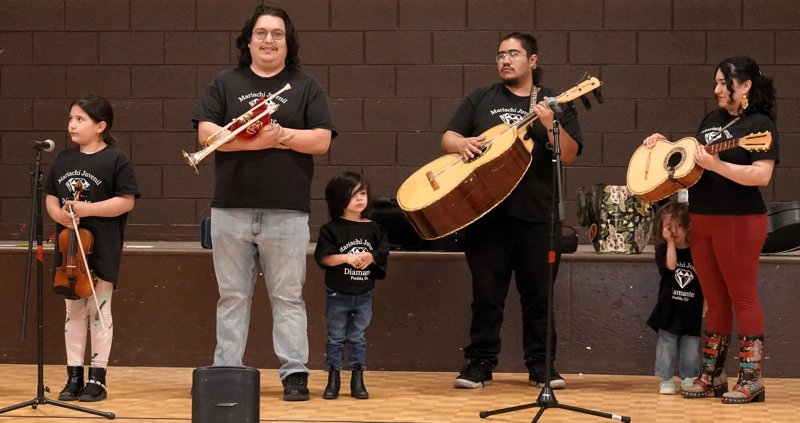 Mariachi musicians perform together onstage with violin, trumpet, guitarrón, and vihuela.