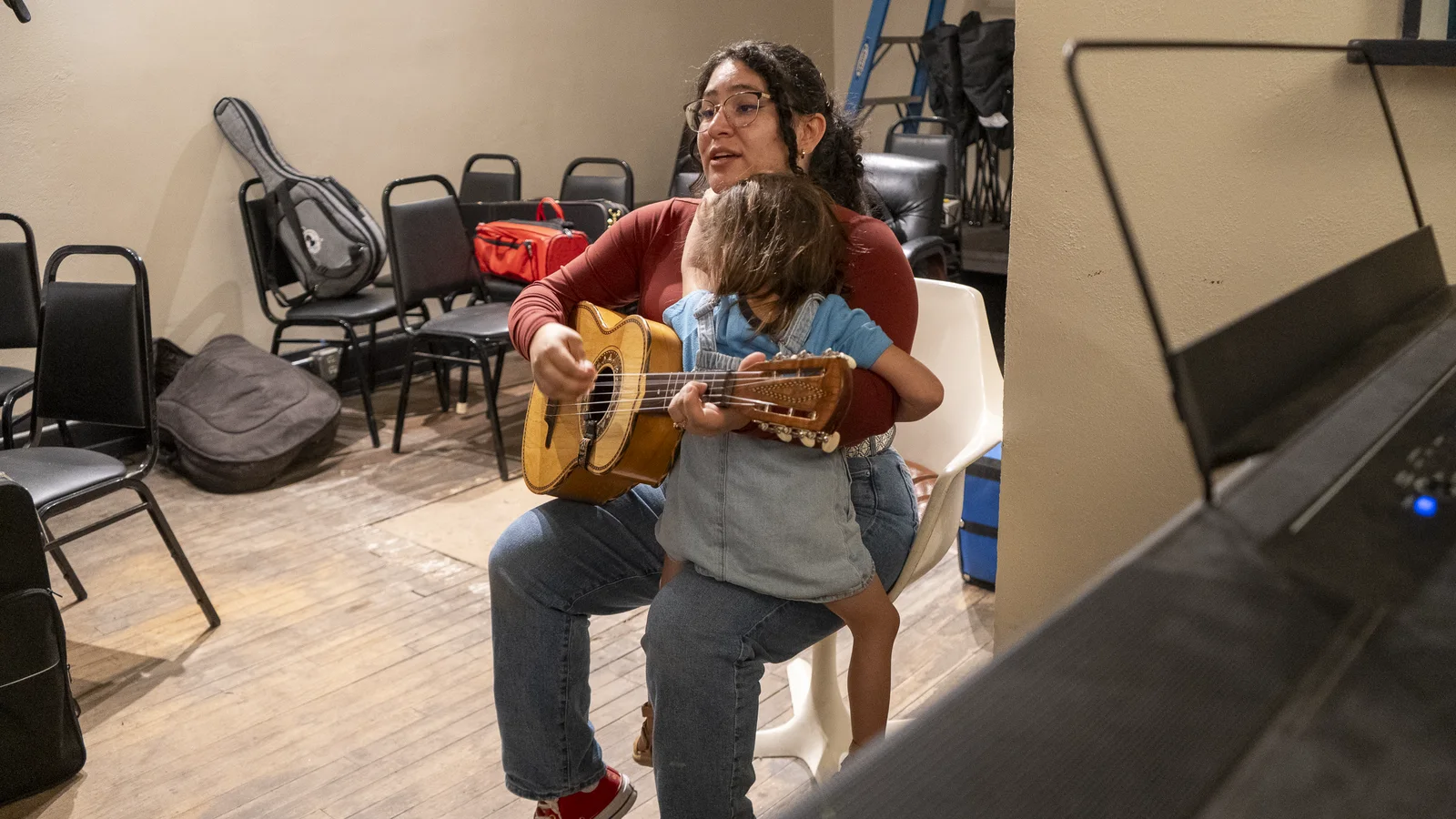 An instructor helps a young student play guitarrón during a mariachi lesson.