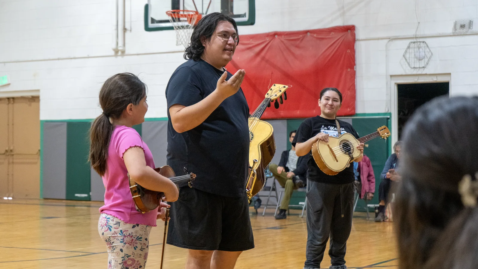An instructor works with a young musician holding a small string instrument while other players watch.