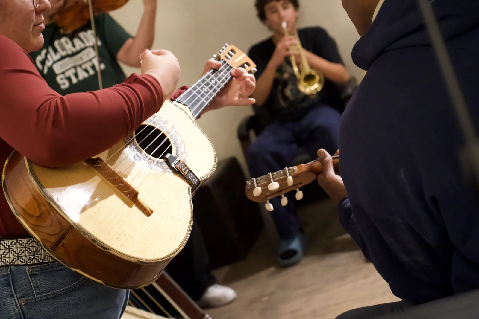 Close-up of musicians playing guitarrón and vihuela with a trumpet player in the background.