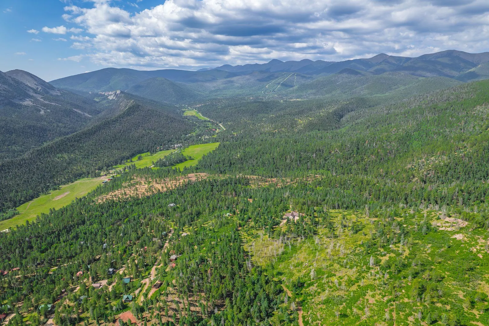 Green Cuchara valley framed by forested mountains beneath a blue sky.