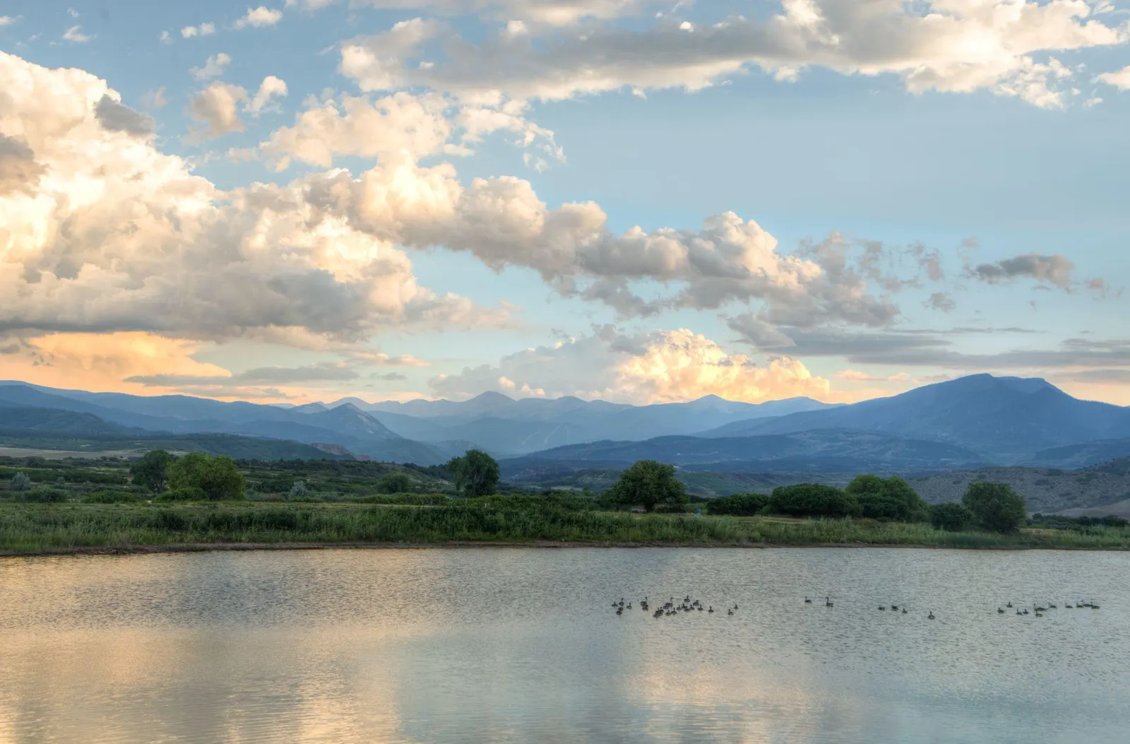 Sunset over a calm lake with the Spanish Peaks in the distance.
