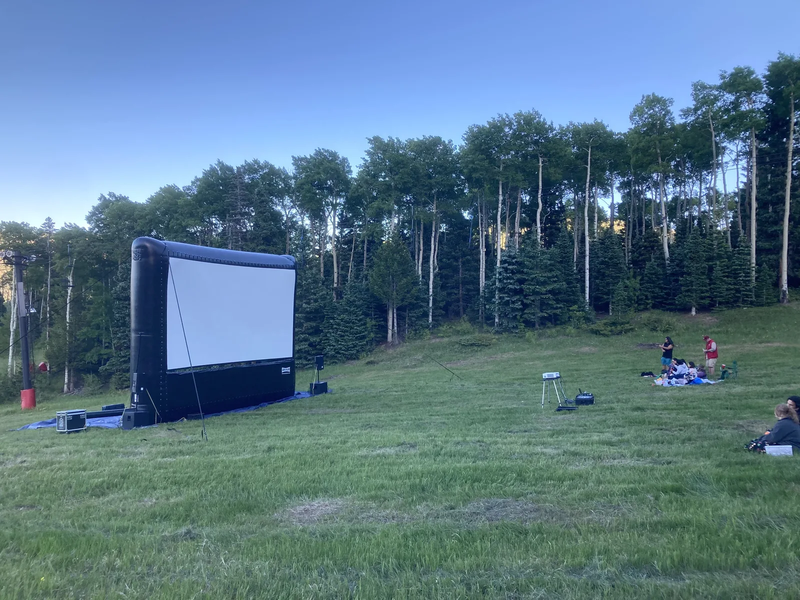 An inflatable movie screen ready for an outdoor screening in a grassy mountain clearing.