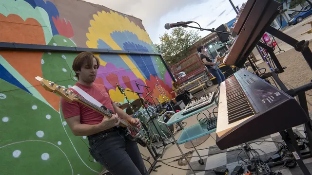 Nash, Vegan Shark's guitarist, performs outdoors beside a keyboard and drum kit in front of a colorful mural.