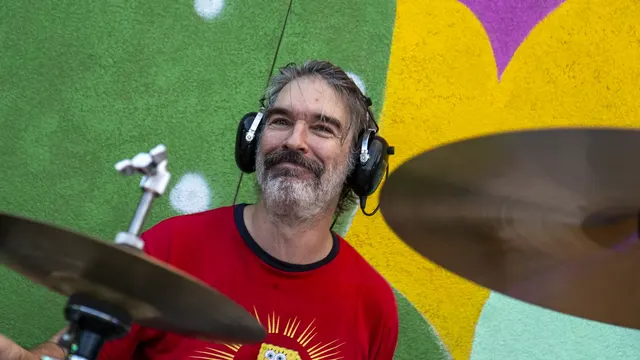 Nathan, Vegan Shark's drummer, wearing headphones and playing in front of a colorful mural.