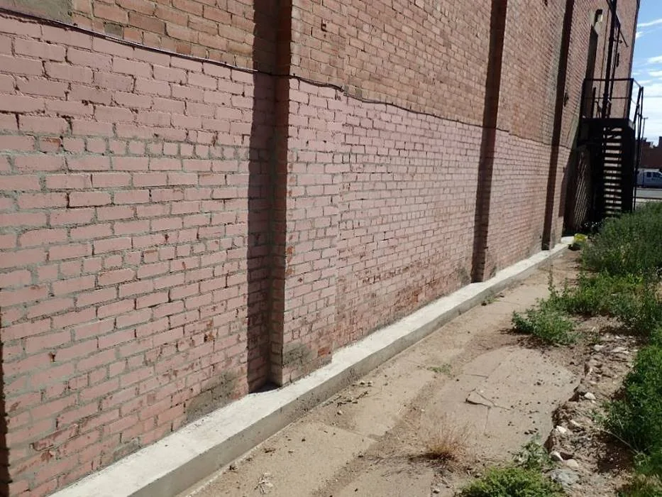 Brick perimeter wall extending below grade with a later concrete strip at its base.