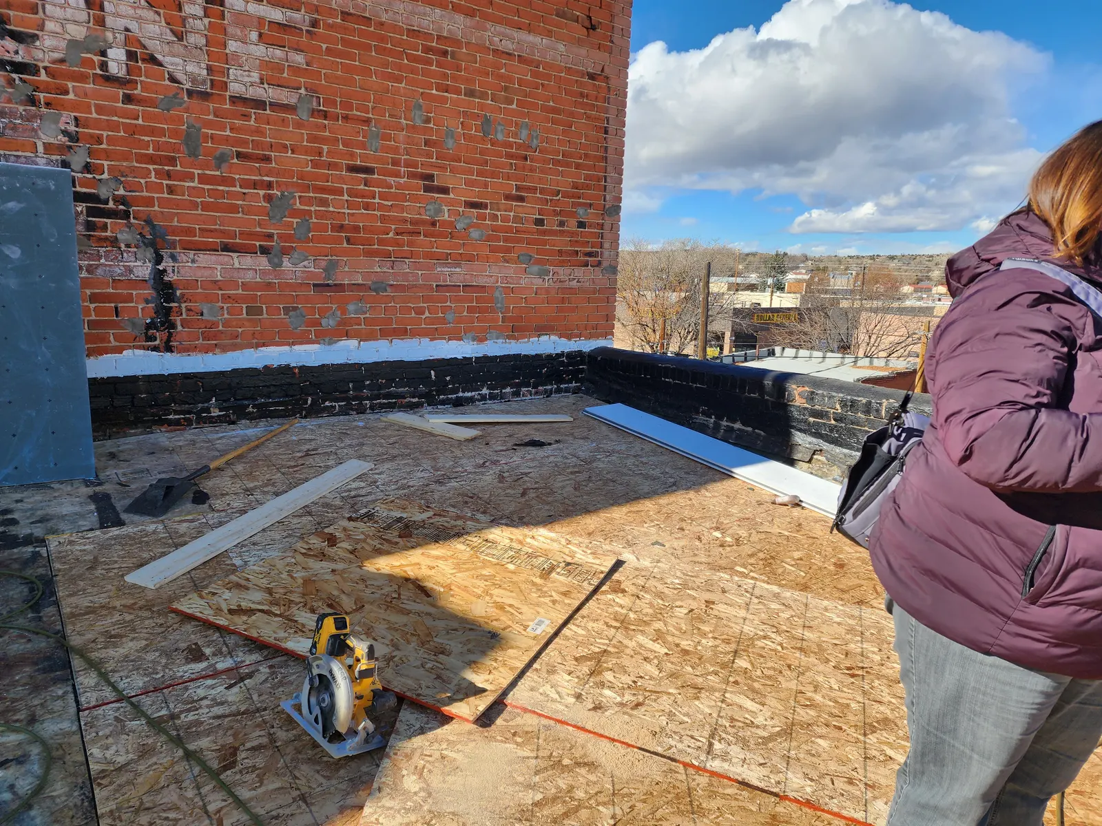 New plywood roof decking fitted beside the historic brick parapet under a blue sky.
