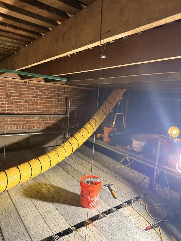 New timber framing beside historic brickwork and a temporary yellow ventilation duct.